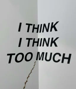 Minimalist black text on a white wall reading I think I think too much, capturing the overthinking patterns driven by subconscious anxiety.