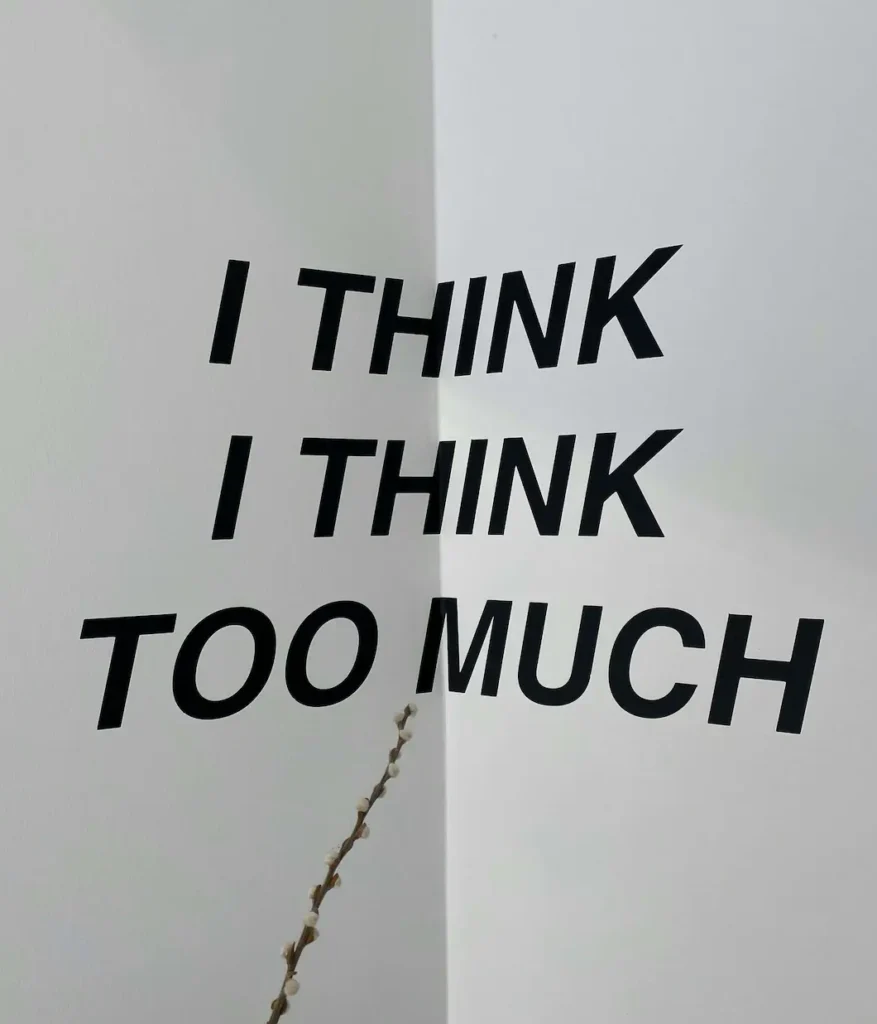 Minimalist black text on a white wall reading I think I think too much, capturing the overthinking patterns driven by subconscious anxiety.