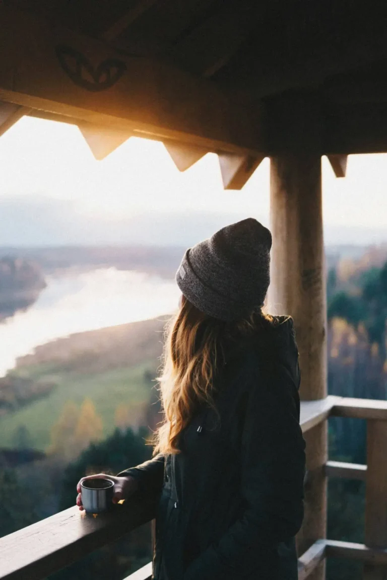 Woman holding a coffee mug while looking at a peaceful landscape during sunrise