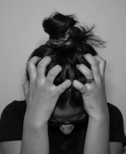 A close-up black and white photograph of a woman holding her head in emotional overwhelm, illustrating the hidden patterns behind emotional triggers behavior.