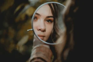 A close-up reflection of a woman's face in a small round mirror, symbolizing self-reflection and an authentic identity shift.