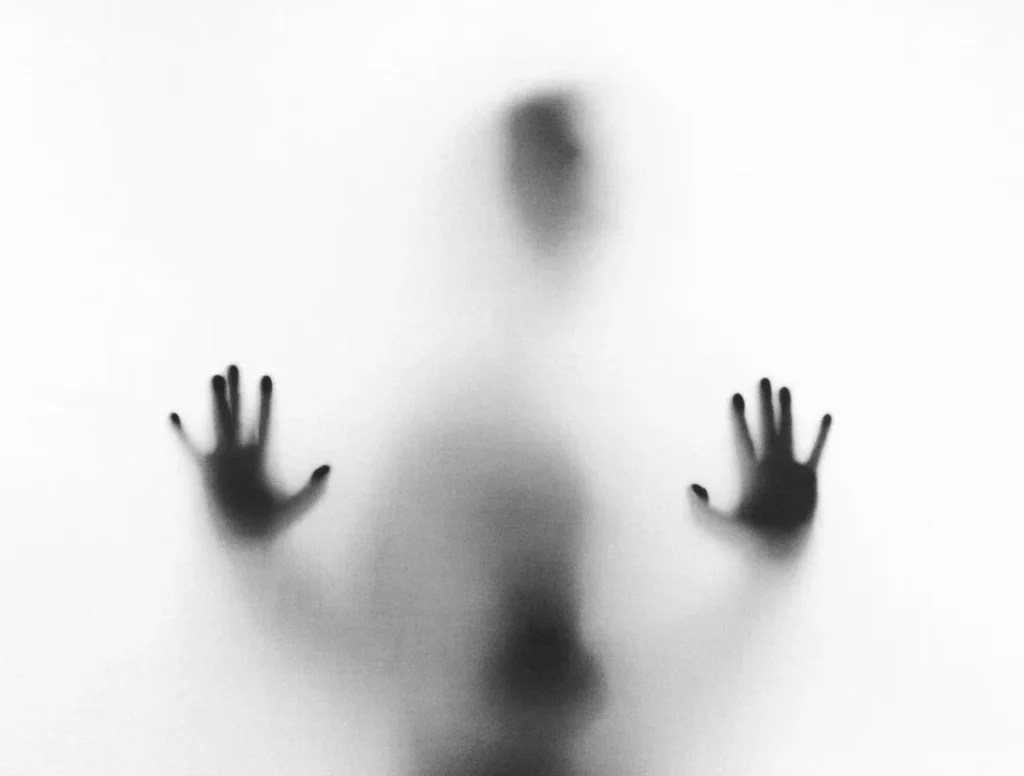 A blurry silhouette of a person pressing their hands against a white wall representing internal mental blocks and self sabotage.