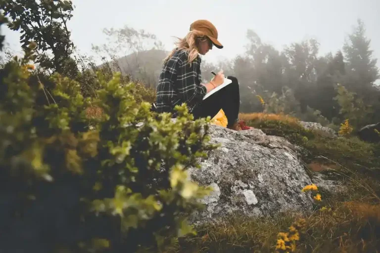 Woman journaling outdoors as she reflects on her thoughts and develops greater self-awareness.