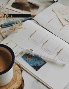 A minimalist handwritten habit tracker bullet journal open on a marble desk next to a warm cup of coffee on a wood coaster, dried flowers, and a pen