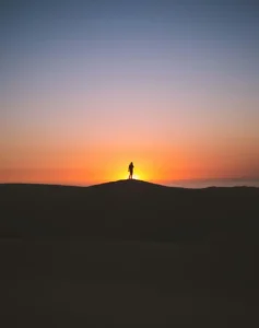 Person standing on a dune at sunrise representing self-sabotage recovery, emotional resilience, and breaking the cycle of self-sabotaging behavior