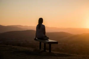 A reflective silhouette of a person sitting peacefully on a bench during a golden sunset, symbolizing breaking the cycle of self-sabotage