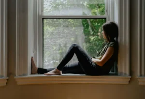 Woman sitting by a window in quiet reflection, representing the inner voice and growing self-awareness.