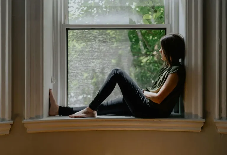Woman sitting by a window in quiet reflection, representing the inner voice and growing self-awareness.