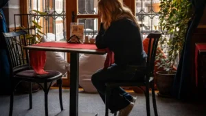 Woman sitting quietly at a café table, reflecting on emotional regulation vs emotional suppression.