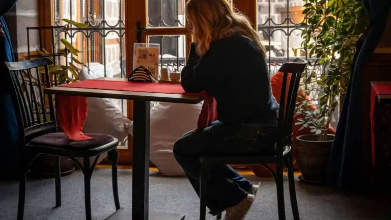 Woman sitting quietly at a café table, reflecting on emotional regulation vs emotional suppression.