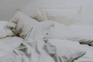 Unmade bed in soft morning light representing waking up feeling tired even after sleeping.