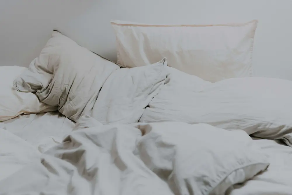 Unmade bed in soft morning light representing waking up feeling tired even after sleeping.