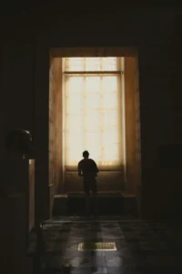 Person standing in a dark space facing a large illuminated opening, representing fear of change and psychological safety