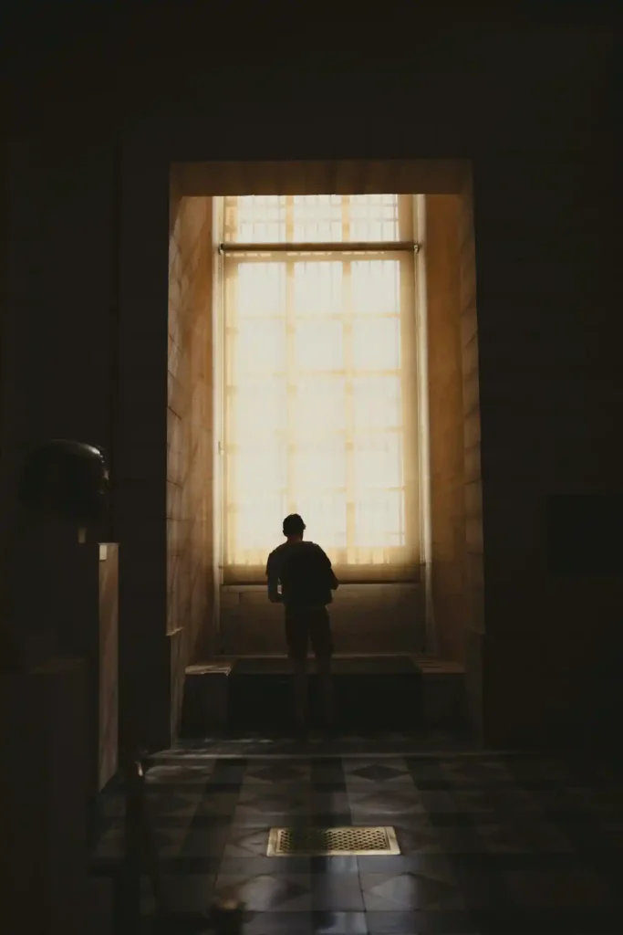 Person standing in a dark space facing a large illuminated opening, representing fear of change and psychological safety