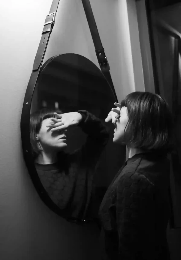 Woman facing her reflection in a mirror, representing self-awareness vs self-consciousness