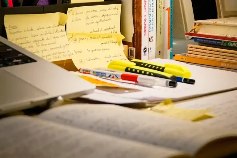 Cluttered study desk with a laptop, notebooks, books, and scattered stationery, illustrating behavioral friction