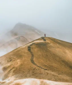 Person standing at the end of a long repeated pathway across a mountain ridge, representing identity and repeated behavior