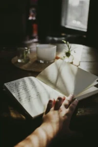 Hand holding an open journal with handwritten entries on one page and a blank page ready for writing.