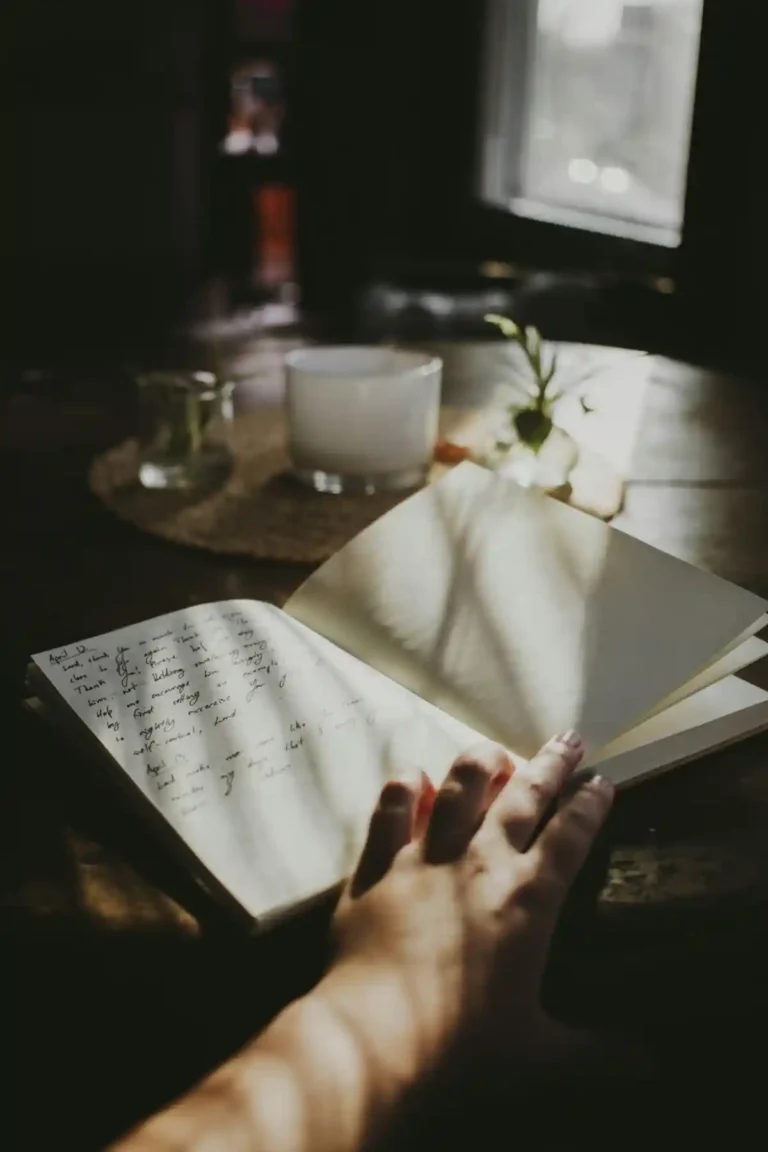Hand holding an open journal with handwritten entries on one page and a blank page ready for writing.