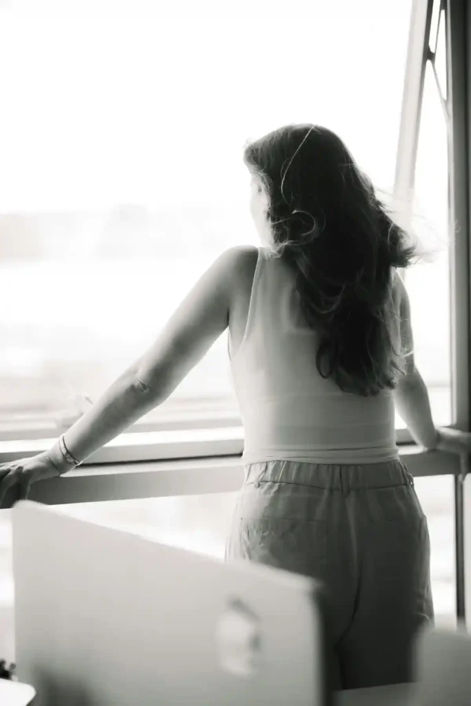 Woman standing by a window, looking outside in a quiet moment of reflection.