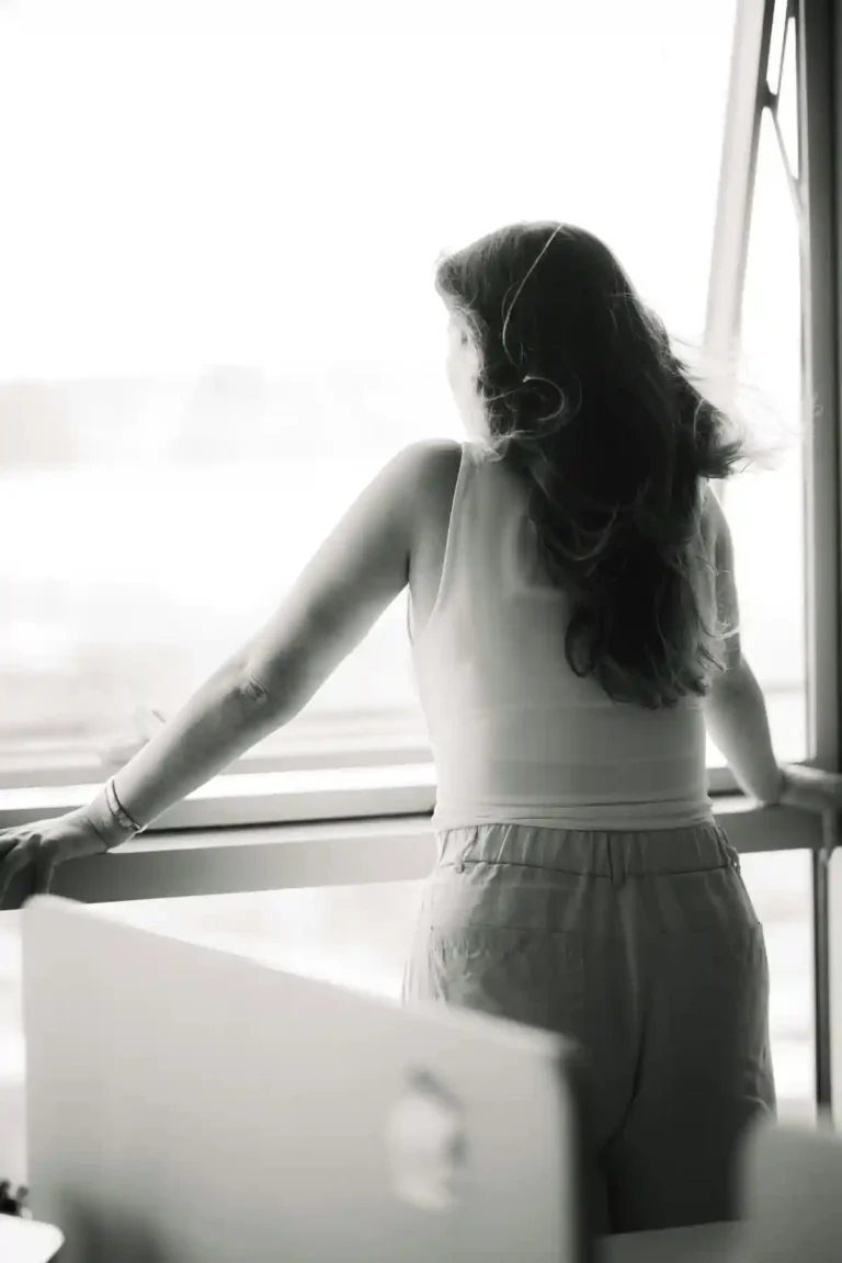 Woman standing by a window, looking outside in a quiet moment of reflection.